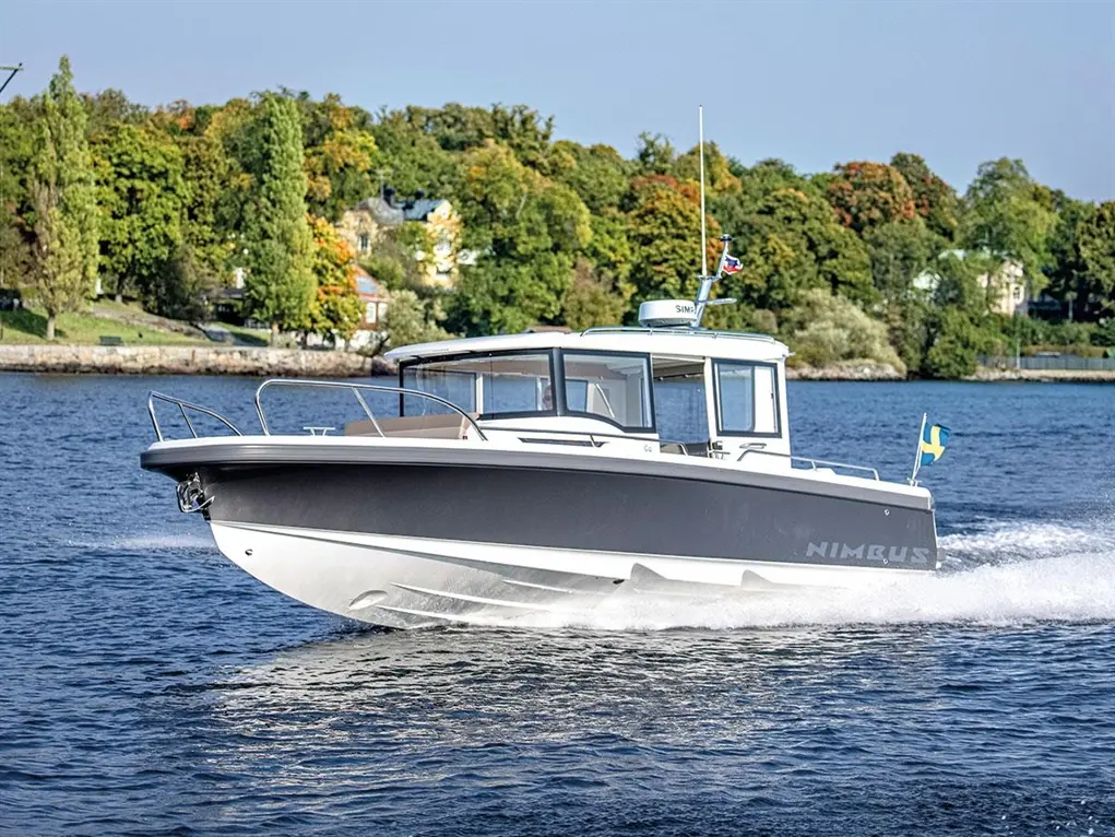 A Nimbus boat cruising on the water, surrounded by trees, with a Swedish flag visible at the stern.